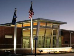 A front view of a building at dusk with the Kansas and American flag posted nearby; the main entrance of the building is clear where viewers can see inside the building.