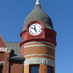 An image of a red and orange clock tower with windows against the backdrop of a blue sky.