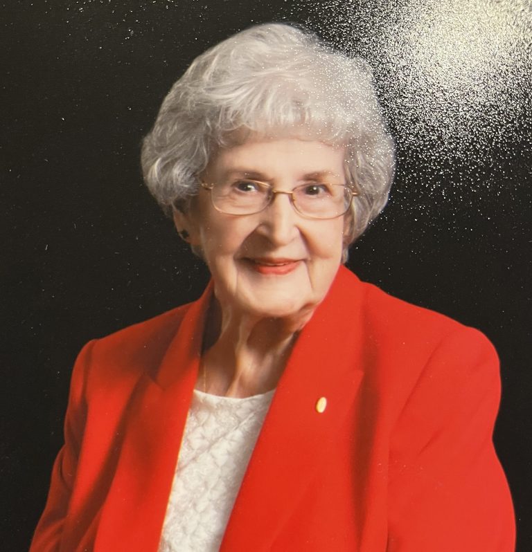 A photo of an elderly woman in a red coat and white shirt.