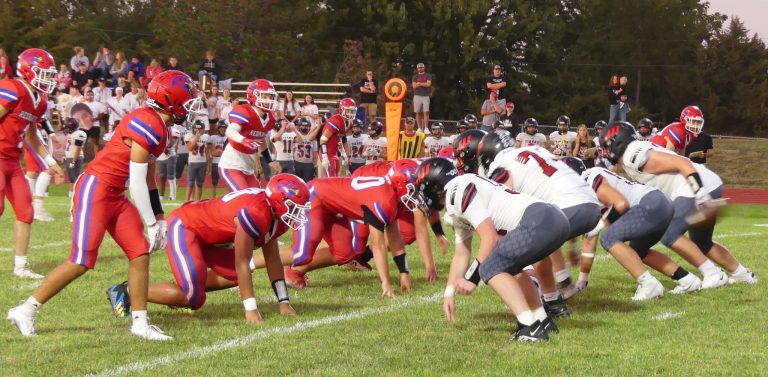 A group of football players in red uniforms faces the other group of football players in white uniforms on a green field.
