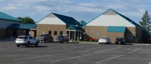 An image of a building and a parking lot with some vehicles during the day.
