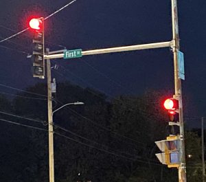 A photo of two flashing red lights of an intersection at night, with trees in the background.