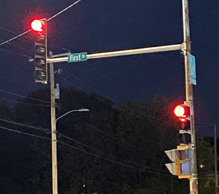 A photo of two flashing red lights of an intersection at night, with trees in the background.