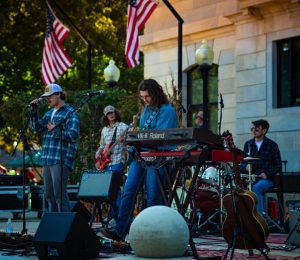 A rock band playing in front of a building with two American flags hanging above.