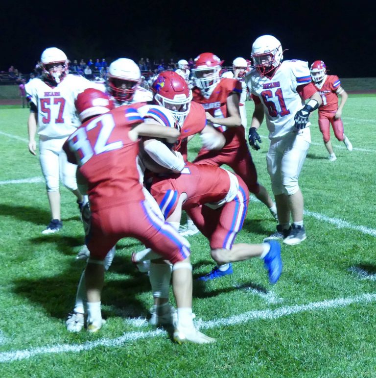 A group of football players in red and football players in white engage in a major tackle on a green football field.