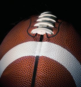 A close up of a brown football in a black background.